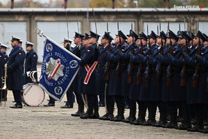 Na zdjęciu kompania honorowa policji w szyku i pozycji baczność. Jeden z policjantów trzyma sztandar jednostki.