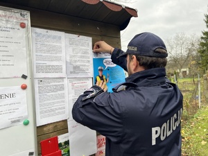 Na zdjęciu policjant wieszający plakat na tablicy informacyjnej.