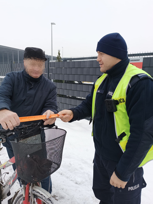 Na zdjęciu policjant drogówki wręcza odblask rowerzyście.