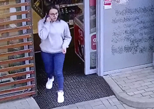 Na zdjęciu kobieta wychodząca ze sklepu ma przy uchu telefon.