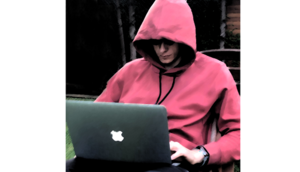 Na zdjęciu młody zakapturzony człowiek przy laptopie.