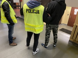 Na zdjęciu dwaj policjanci w kamizelkach z napisem Policja, po prawej zatrzymany.