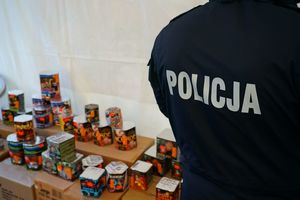 Na zdjęciu widzimy plecy policjanta - napis policja w tle fajerwerki na stoliku