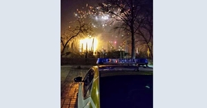 Na zdjęciu na pierwszym planie policyjny radiowóz, w tle wybuchające fajerwerki.