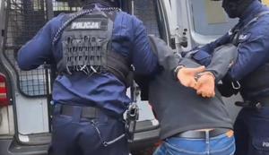 nA ZDJĘCIU DWÓCH POLICJANTÓW WPROWADZA DO RADIOWOZU SKUTEGO KAJDANKAMI ZATRZYMANEGO.