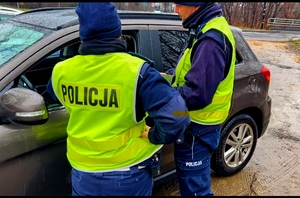 Na zdjęciu policjanci drogówki stojący przy zatrzymanym samochodzie. Rozmawiają z kierowcą.