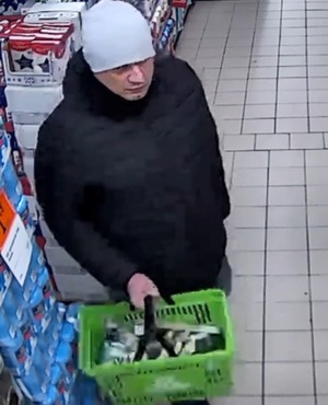 Na zdjęciu mężczyzna w czapce zimowej w sklepie, w prawej ręce trzyma koszyk z zakupami.