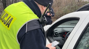Na zdjęciu policjant kontroluje zatrzymany samochód.