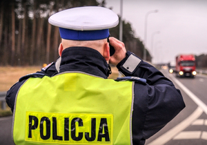 Na zdjęciu policjant drogówki patrzący na drogę przez lornetkę