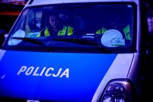 Na zdjęciu przód policyjnego radiowozu typu furgon. Widach za szybą dwóch policjantów.