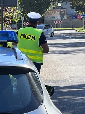 Policjant przy radiowozie a w tle zawracający samochód.