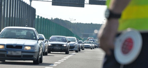 na zdjęciu widzimy zatłoczoną drogę i tarczę policyjną trzymaną przez policjanta