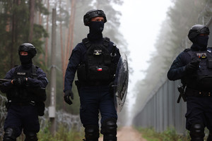 Na zdjęciu trzej policjanci idą wzdłuż granicznego płotu