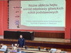 Na zdjęciu aula, widać słuchaczy, widać policjanta przemawiającego do audytorium, w tle ekran a na nim napis &quot;objawy hejtu w gliwickich szkołach&quot;