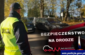 Na zdjęciu policjant patrzący w rejon parkujących aut przy cmentarzu. Widać po prawej płonący znicz charakterystyczny dla tego święta.