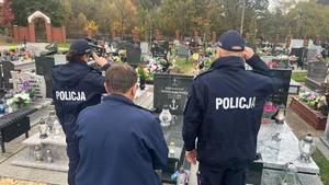 Na zdjęciu policjant i policjantka oraz ksiądz kapelan między nimi oddają honor przed nagrobkiem.