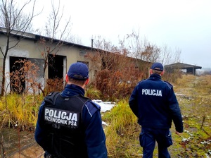 Na zdjęciu dwóch policjantów idących wzdłuż pustostanu