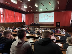 Na zdjęciu aula wypełniona słuchaczami. Na scenie wyświetlany jest slajd z napisem Debata. Widać siedzących tam prelegentów.