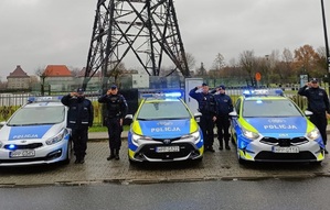 Na zdjęciu trzy radiowozy, obok salutujący policjanci w tle gliwicka radiostacja.