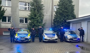 Naz zdjeciu trzy radiowozy przy knurowskim komisariacie, obok salutujący policjanci.