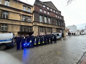 Na zdjęciu kilkunastu policjantów stojących przed budynkiem komendy w geście salutowania.