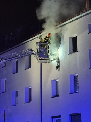 Na zdjęciu strażak w wysięgniku dźwigu przy płonącym oknie mieszkania.