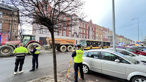 Na zdjęciu widzimy policjantów dokonujacych pomiarów i oględzin miejsca wypadku. w tle traktor i rozbity z przodu autobus.