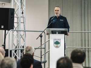 na zdjęciu przy mównicy oficer policji przemawiający do słuchaczy.