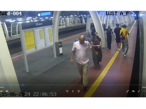 Na zdjęciu mężczyzna stojący na peronie dworca w różowej koszuli i jasno niebieskich spodniach