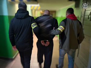 Zatrzymany mężczyzna prowadzony przez dwóch nieumundurowanych policjantów.