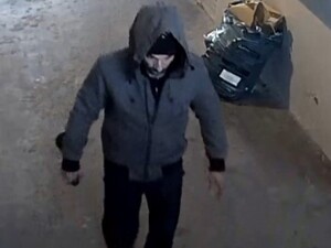 mężczyzna w szarej kurtce idący drogą, w kapturze na głowie