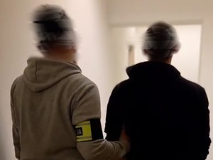 Na zdjęciu od tyłu policjant w ubraniu cywilnym z opaską na ręku z napisem POLICJA, prowadzi zatrzymanego