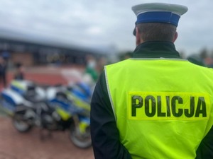 Umundurowany policjant stojący tyłem w kamizelce odblaskowej.