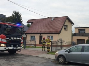 Na ulicy stojący pojazd osobowy oraz samochód straży pożarnej. W tle stojące budynki.
