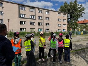 Uczniowie przed egzaminem na kartę rowerową stojący z policjantem na rowerowym miasteczku ruchu drogowego