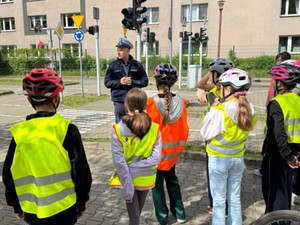 Policjant stojący wraz z uczniami na miasteczku ruchu drogowego.