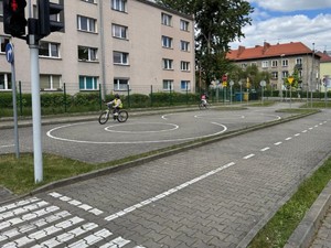 Uczniowie na miasteczku ruchu drogowego podczas praktycznego egzaminu na kartę rowerową pod okiem policjanta ruchu drogowego.