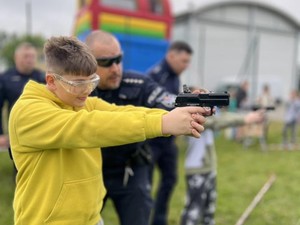 chłopiec mierzy z atrapy pistoletu do tarczy pod okiem policjanta