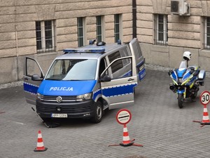Na dziedzińcu sądu stoi radiowóz oznakowany oi  motocykl wraz ze słupkami w kolorze czerwono białym