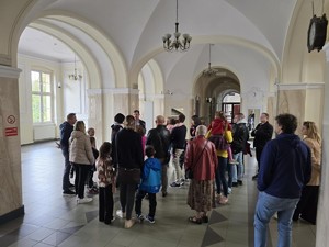 Grupa zwiedzających stoi na korytarzu sosnowym, wysłuchują wykładu przewodnika.