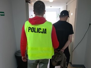 Policjant w kamizelce prowadzi zatrzymanego.