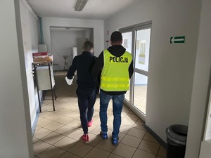 Policjant w kamizelce prowadzi zatrzymanego.