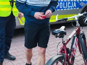 Na zdjęciu mężczyzna stojący przy rowerze. W tle policjant i radiowóz.