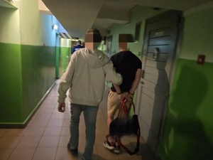 Nieumundurowany policjant prowadzi zatrzymanego korytarzem w policyjnym areszcie.