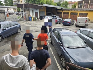 Na parkingu samochodowym policjanci prowadzą zatrzymanych do samochodu.