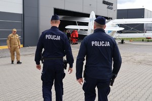 Dwóch umundurowanych policjantów idących w kierunku hangaru.