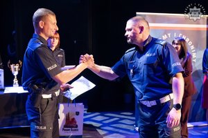 Na zdjęciu policjant odbierający nagrodę na scenie w konkursie od innego mundurowego.