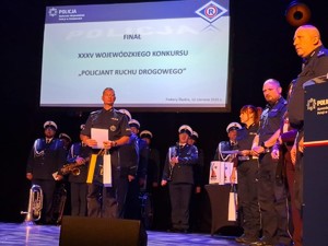Na scenie ceremonia wręczenia nagród. Stoją zarówno policjanci jak i orkiestra Policyjna.