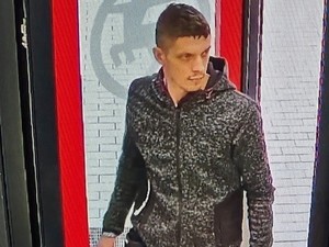 Na zdjęciu młody mężczyzna w szarej bluzie z kapturem i w ciemnych spodniach dresowych.