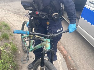 Na zdjęciu widać rower, który trzyma policjant. W tle oznakowany radiowóz